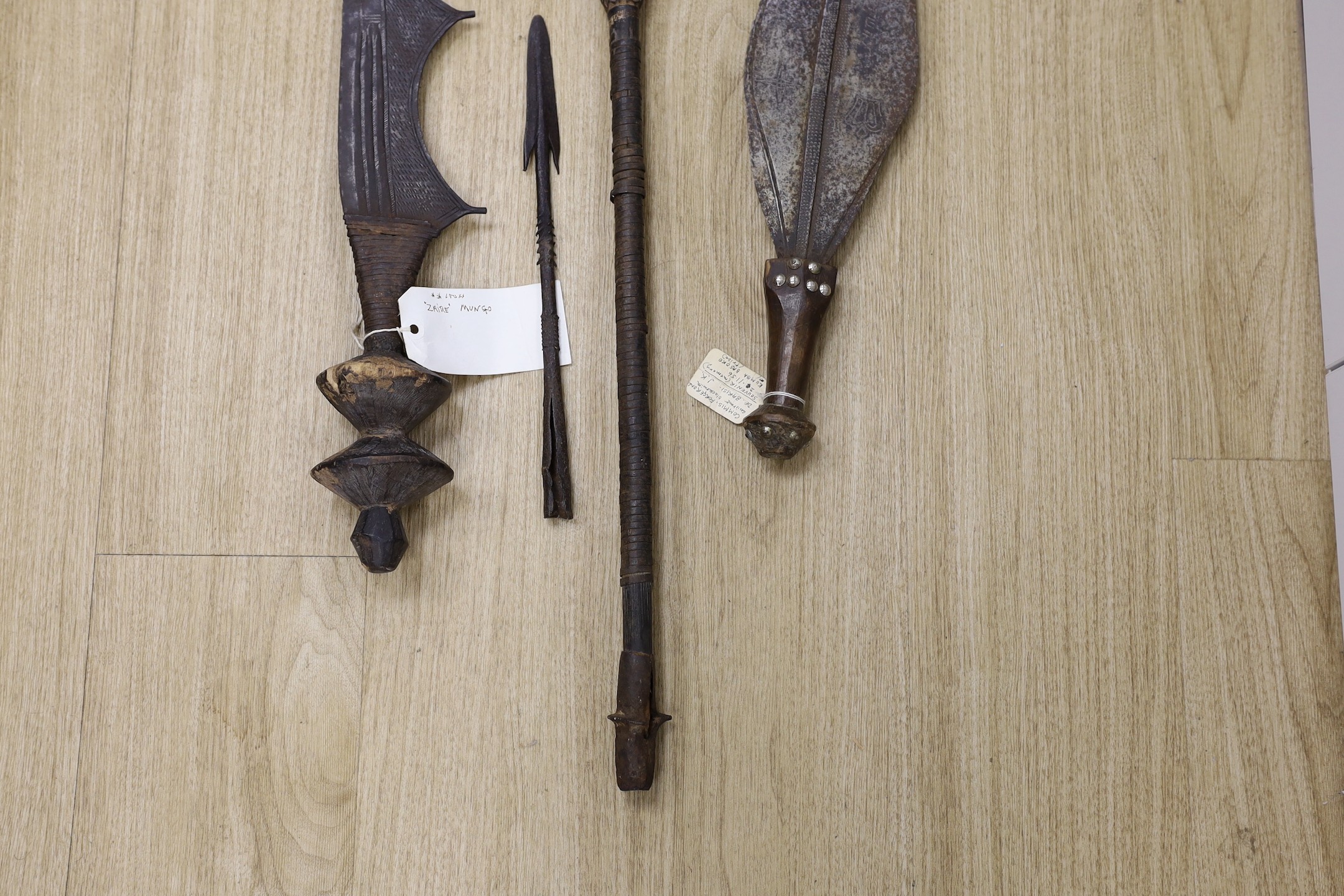 A group of African tribal weapons including an Ngombe ceremonial sword, a similar spear, Democratic Republic of Congo, a Kuba sword and a spear head, spear length 148.5cm